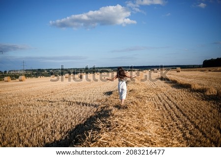 Portrait of a young curly-haired woman in a wheat field, where wheat is mowed and sheaves are standing, enjoying nature. Nature. sun rays Agriculture