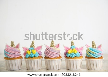 Many cute sweet unicorn cupcakes on white wooden table