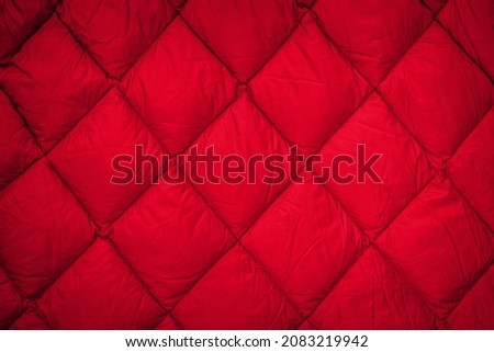Modern quilted pattern on Warm winter jacket. Red Down jacket cloth background. Red blanket fabric or puffer jacket texture.