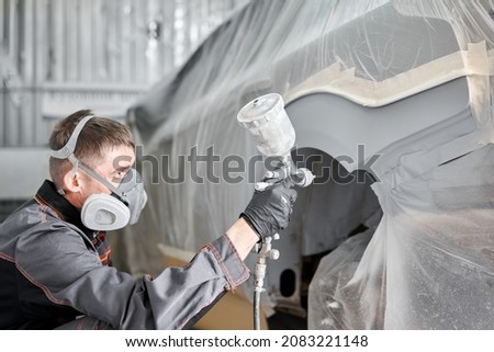 Painting the rear part of the car. Car painter wearing costume and protective gear. Car service station. Restoring a car after an accident Royalty-Free Stock Photo #2083221148