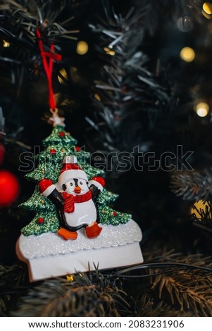 Christmas toy figurine of funny penguin in a Santa Claus hat hanging on the Christmas tree branches. New Year festive magic details