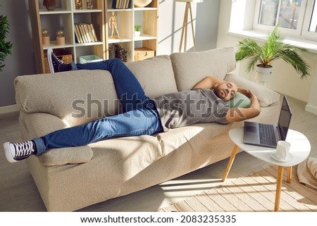 Lazy man enjoying a nap. Tired man sleeping on the sofa at home. Young guy falls asleep on the couch while working on his laptop computer in the living room Royalty-Free Stock Photo #2083235335