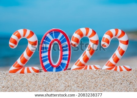 New Year's bright funny numbers 2022 in stripes, against the background of the beach and the sea, selective focus.Creative New Year and Christmas card.Tourism, recreation and travel concept. Close-up.