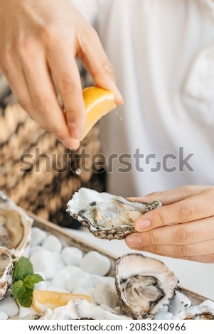 A man's hands squeezes fresh lemon juice onto an raw opened oyster, lifestyle food, ready to eat. Oyster dinner with champagne in restaurant. Royalty-Free Stock Photo #2083240966
