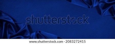 Beautiful dark blue silk satin background. Soft folds on shiny fabric. Luxury background with copy space for text, design. Wide banner. Flat lay, table top view. Birthday, Christmas, Valentine.
