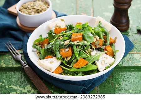 Warm salad with arugula, baked pumpkin, cheese and pumpkin seeds on a rustic background, selective focus