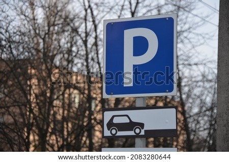 Parking sign on the background of trees without leaves and a brick house