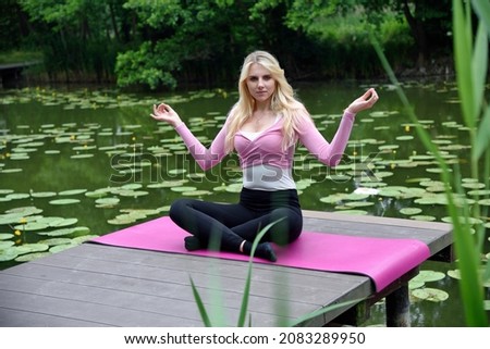 Young and slim woman exercising in park with pond. Polish woman doing some yoga and stretching. 