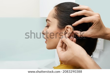 Installation hearing aid on woman's ear at hearing clinic, close-up, side view. Deafness treatment, hearing solutions Royalty-Free Stock Photo #2083290388