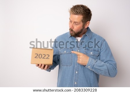 Young excited casual man pointing finger side showing calendar isolated over white background.