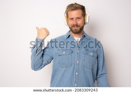 Young smiling casual man wearing headphones showing thumb up isolated over white background.