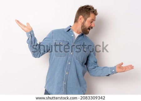 Young funny man wearing denim shirt showing product space with hand isolated over white background.