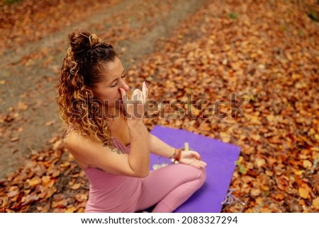 woman performing Nadi Shodhana Pranayama or Alternate Nostril Breathing. Latin girl doing yoga in the forest. Royalty-Free Stock Photo #2083327294