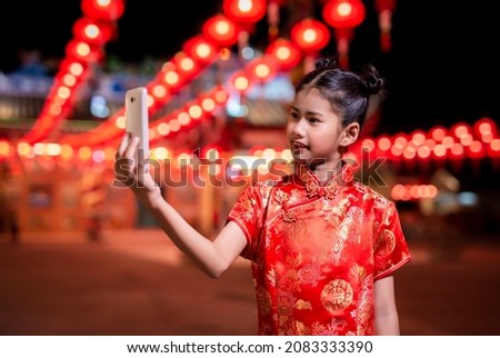 Cute little Asian girl in chinese traditional red dress taking a selfie with smartphone for Chinese New Year