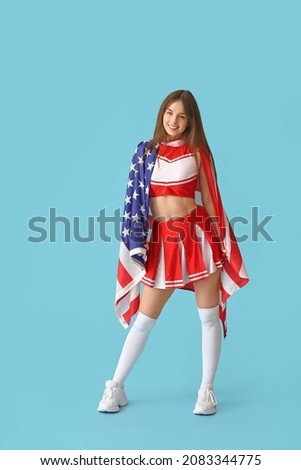 Beautiful young cheerleader with USA flag on color background