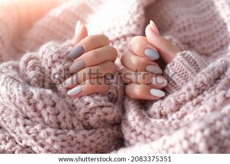 Women's hands with a beautiful matte oval manicure in a warm purple knitted sweater. Winter trend, polish beige nails with gel polish, shellac. Copy space.