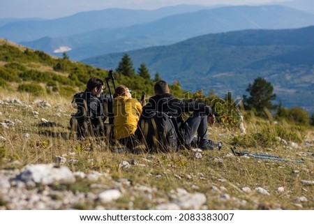 Outdoor shot of young hikers sitting together taking a break on hike. Caucasian man and woman sitting, talking and enjoying the view on a hike on maountain while taking pictures.