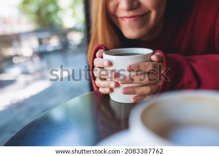 Closeup image of a young woman holding and drinking hot coffee