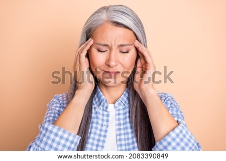 Photo of upset tired retired woman wear plaid shirt arms temples closed eyes headache isolated beige color background
