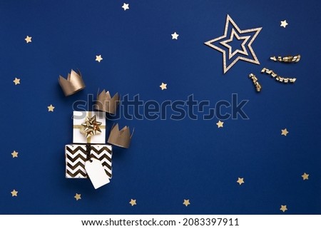 Traditional Three King's Day of January 6. Three gold crowns and festive gift boxes on blue background with winter decorations. Happy Epiphany day. Top view, copy space, flat lay.