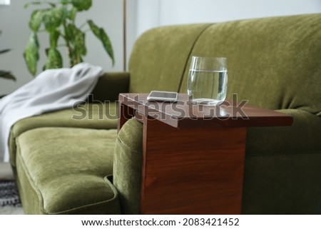 Glass of water with mobile phone on armrest table in room Royalty-Free Stock Photo #2083421452
