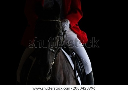 A rider in red jacket on horseback riding on dark background. Sportman on black horse isolated on black background.