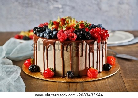 Birthday cake in chocolate with strawberries, blueberries and cherry on wood background. Picture for a menu or a confectionery catalog.
