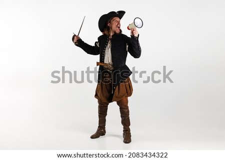 Portrait of man, pirate in vintage costume raising sword and shouting in megaphone isolated over white background. Combination of medeival and modern styles. Concept of history. Copyspace for ad.