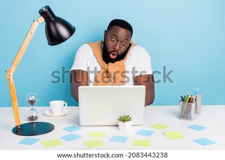 Photo of shocked guy sit table pc hold phone call open mouth bet wear t-shirt jumper front-tie isolated blue color background