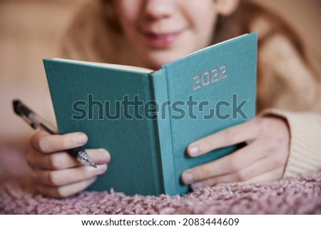 Close Up Of Teenage Girl Lying On Bed At Home Writing Resolutions In New Year 2022 Diary  Royalty-Free Stock Photo #2083444609