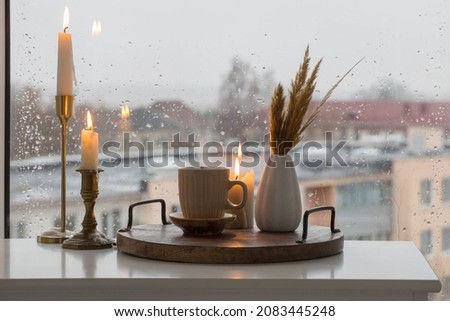 autumn still life with burning candles and a cup of coffee on the background of a window with raindrops