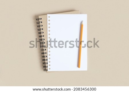 Notebook with pencil. School notebook on neutral beige background, spiral notepad on table. Top view of open notebook with blank pages, office notepad flat lay. White Page for your write. Copy Space.