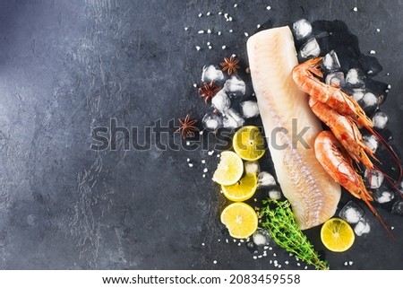 Cod shrimp background. White fish fillet, frozen shrimps on a dark background with lemon, ice, anise and thyme. Background for your pages
