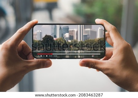 Online movie streaming with smartphone. Young man watching a movie on a mobile phone with an imaginary video player service. Royalty-Free Stock Photo #2083463287