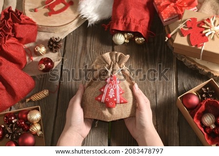 Woman's hands hold Christmas gift on wooden table next to other toys and gifts. Authentic close-up Christmas photo. Preparation for the holiday. Craft gifts. DIY. Advent. Cozy Holiday at home