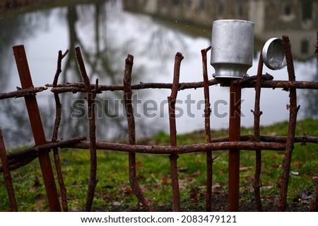 Metal can on the fence. Rural landscapes, traditional old clay pots on a wicker fence. metal milk container on the fence, a village tradition. Royalty-Free Stock Photo #2083479121
