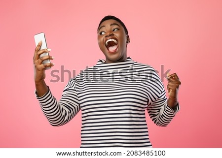 Joyful Overweight African American Female Using Phone And Gesturing Yes Celebrating Success Standing Over Pink Studio Background. Great News, Victory Concept Royalty-Free Stock Photo #2083485100