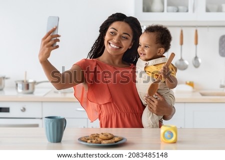 African American Mother Taking Selfie With Her Little Baby On Smartphone In Kitchen Interior, Happy Black Woman Making Photos With Cute Infant Child At Home, Enjoying Spending Time Together