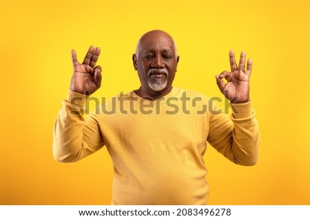 Stress relief concept. Edlerly African American man meditating with closed eyes, keeping calm on orange studio background. Senior black male practicing yoga, searching for inner balance