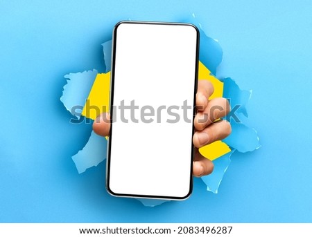 Mobile App Promo, Great Offer. Closeup of hand holding smartphone with white empty screen showing device close to camera breaking through blue paper sheet. Blank display with free copy space, mock up