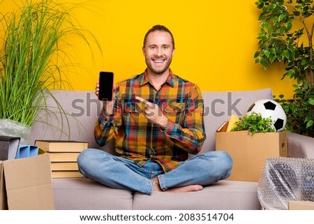 Photo of nice guy sit divan indicate forefinger phone touchscreen wear checkered shirt isolated yellow color background
