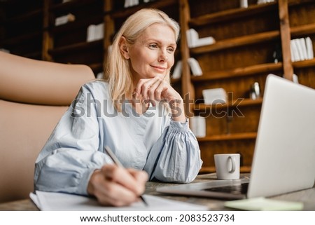 Smart caucasian mature middle-aged businesswoman CEO boss leader teacher writing, taking notes on laptop, e-learning , working remotely online in home office Royalty-Free Stock Photo #2083523734