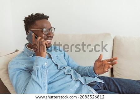 Young man using a cellphone while relaxing at home. Happy African American man using phone texting and browsing internet sitting on sofa. Black male networking in social media using app on mobile.