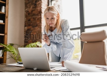 Concentrated caucasian middle-aged mature businesswoman ceo boss typing on laptop, working at office desk with documents, searching surfing web online Royalty-Free Stock Photo #2083529698