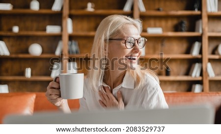 Laughing cheerful middle-aged mature businesswoman CEO leader teacher tutor freelancer working on laptop on distance online, drinking hot beverage, watching webinars from home office