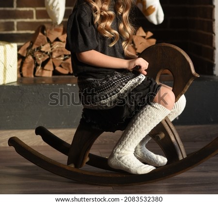a girl in warm knee socks sits on a wooden horse