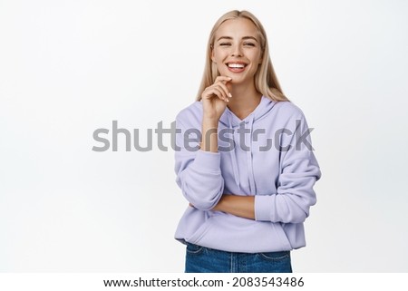 Stylish modern girl with blond long haircut, smiling at camera, looking confident, standing over white background