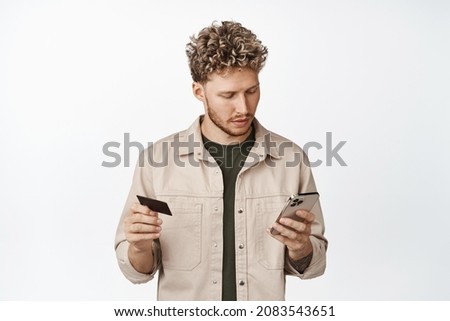 Online shopping. Young handsome man placing order, using mobile phone app and credit card, paying with application, standing over white background