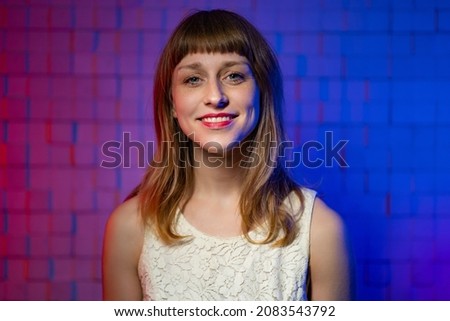 Pretty young caucasian woman with blond hair with bangs. The concept of natural female beauty. Portrait of singer in recording studio against background of soundproof wall with red and blue lighting Royalty-Free Stock Photo #2083543792