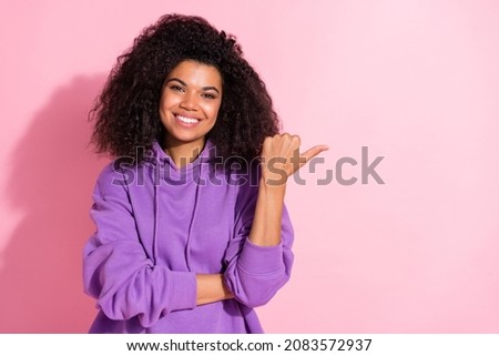 Photo of pretty charming afro girl wear violet sweatshirt pointing thumb empty space smiling isolated pink color background